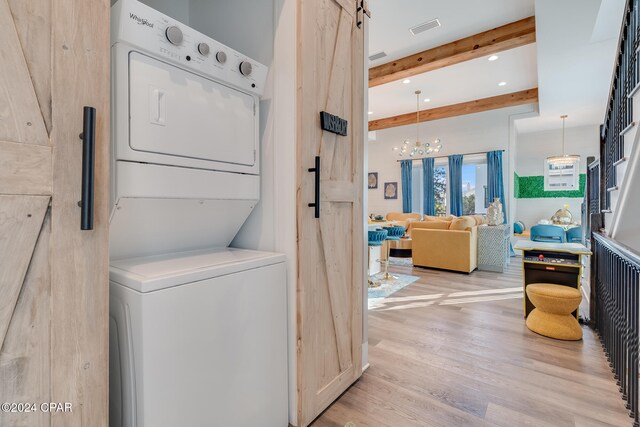 washroom featuring a barn door, light wood-type flooring, stacked washing maching and dryer, and a chandelier