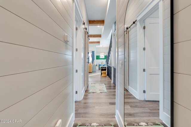 hall with light wood-type flooring, beam ceiling, and a barn door