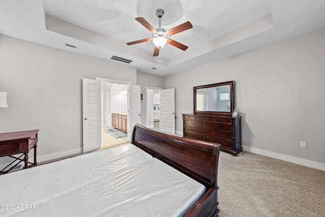 carpeted bedroom with a raised ceiling, ensuite bathroom, and ceiling fan