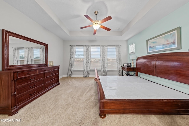 carpeted bedroom with ceiling fan and a tray ceiling