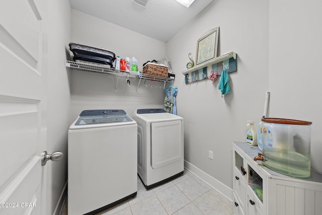 clothes washing area featuring washer and clothes dryer, cabinets, light tile patterned floors, and a textured ceiling