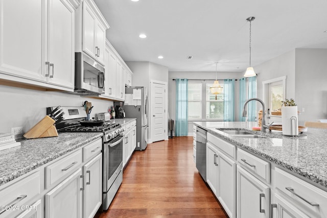 kitchen featuring light stone counters, stainless steel appliances, sink, white cabinets, and hanging light fixtures