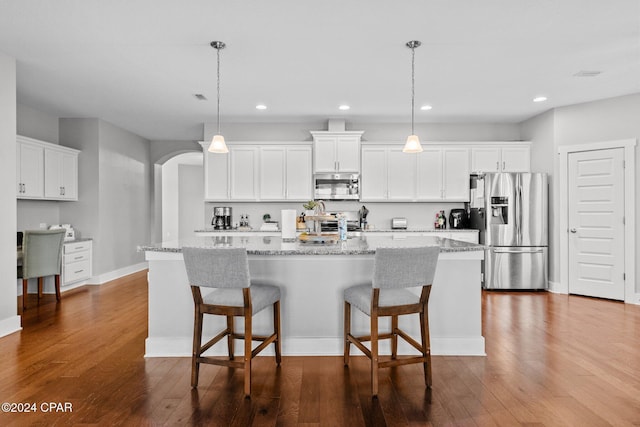 kitchen with pendant lighting, light stone countertops, an island with sink, appliances with stainless steel finishes, and white cabinetry