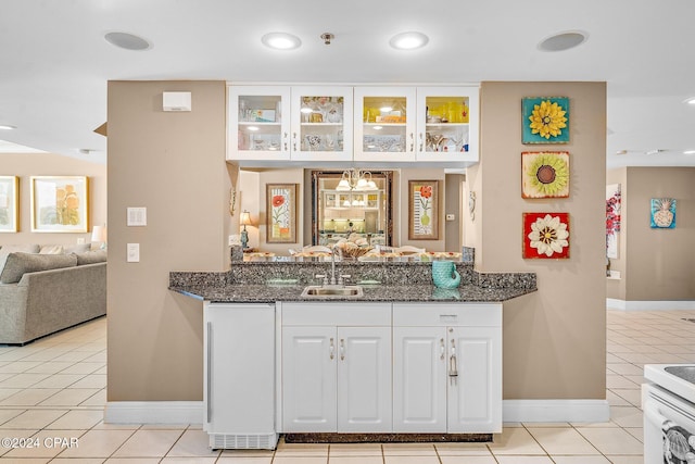 kitchen with dark stone counters, sink, light tile patterned floors, white cabinets, and range