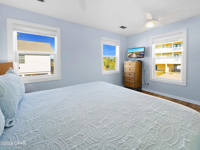 bedroom with ceiling fan, visible vents, baseboards, and wood finished floors