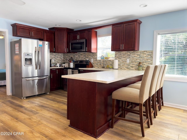 kitchen featuring light countertops, appliances with stainless steel finishes, a peninsula, light wood-style floors, and reddish brown cabinets