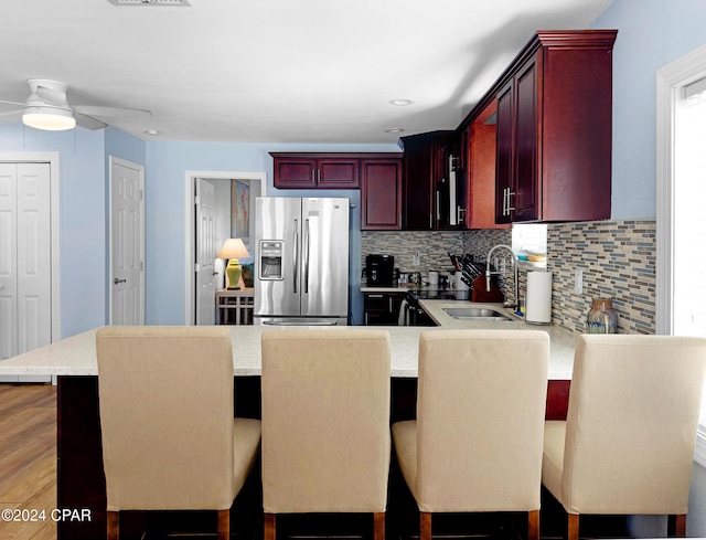 kitchen with a ceiling fan, a peninsula, reddish brown cabinets, stainless steel fridge, and backsplash