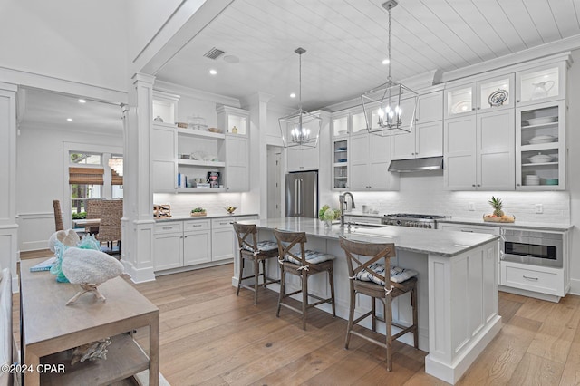 kitchen featuring high end fridge, built in microwave, a kitchen island with sink, sink, and decorative light fixtures