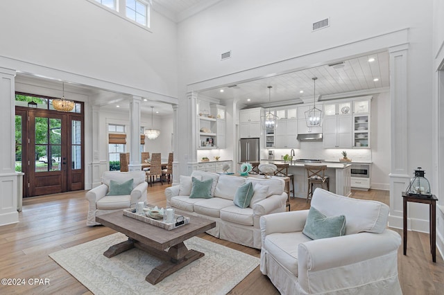 living room with ornate columns, crown molding, light hardwood / wood-style flooring, and a high ceiling