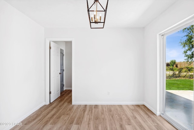 spare room featuring a notable chandelier and light hardwood / wood-style floors