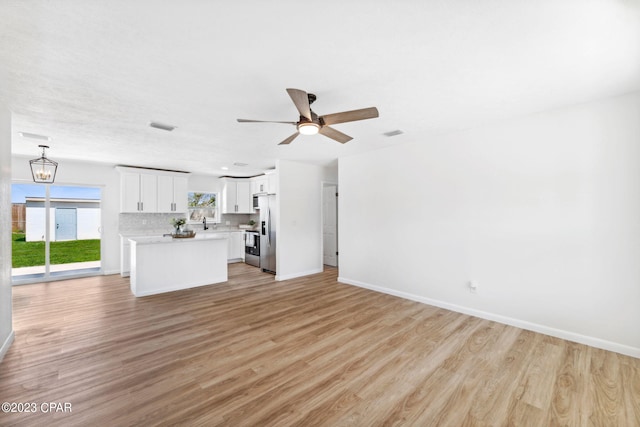 unfurnished living room featuring ceiling fan with notable chandelier and light wood-type flooring