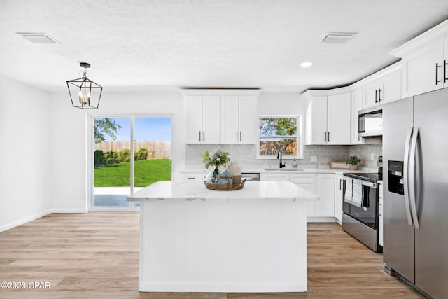 kitchen with stainless steel appliances, sink, pendant lighting, white cabinets, and a kitchen island