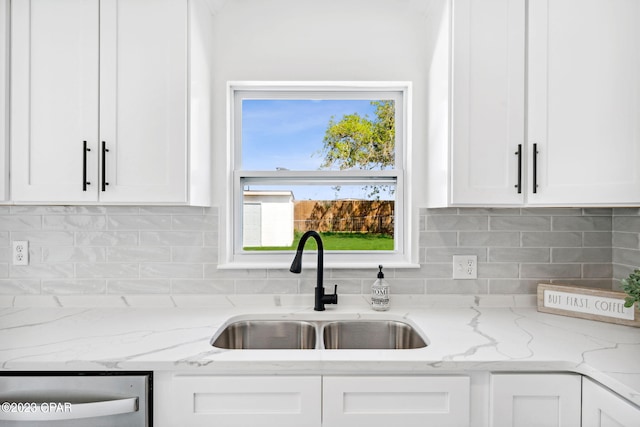 kitchen featuring decorative backsplash, light stone counters, stainless steel dishwasher, sink, and white cabinets