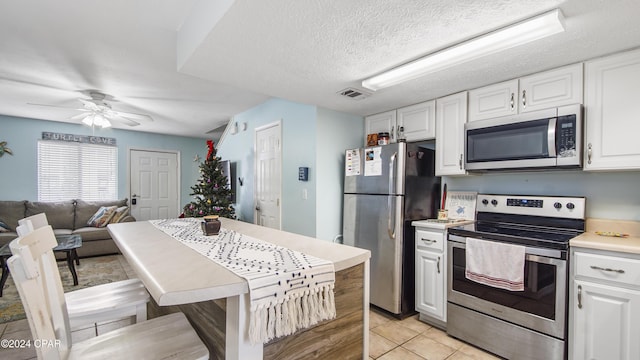 kitchen with a textured ceiling, stainless steel appliances, light countertops, and white cabinets