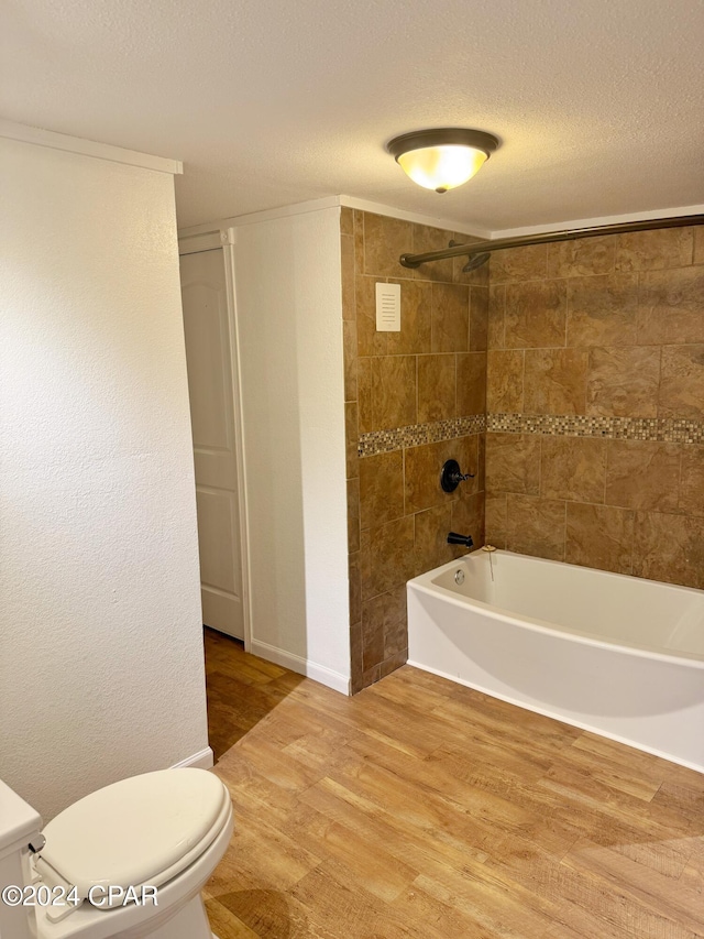 bathroom with tiled shower / bath, hardwood / wood-style floors, a textured ceiling, toilet, and ornamental molding