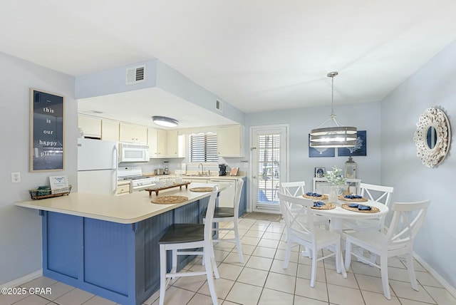 kitchen with a peninsula, white appliances, visible vents, light countertops, and decorative light fixtures