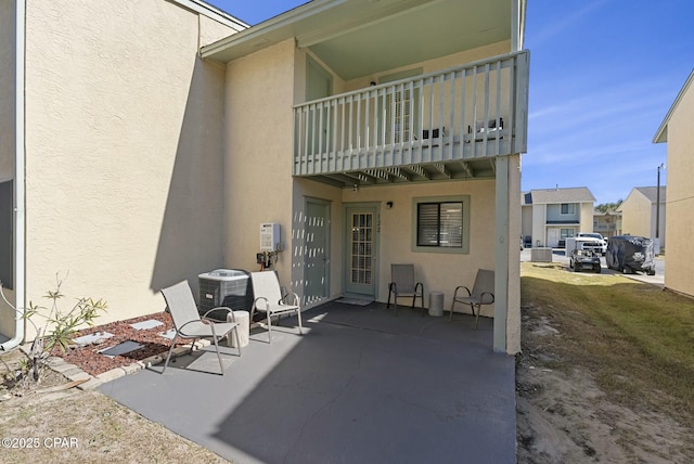 rear view of property with a balcony, central AC unit, a patio, and stucco siding