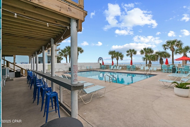 community pool with fence, a bar, and a patio