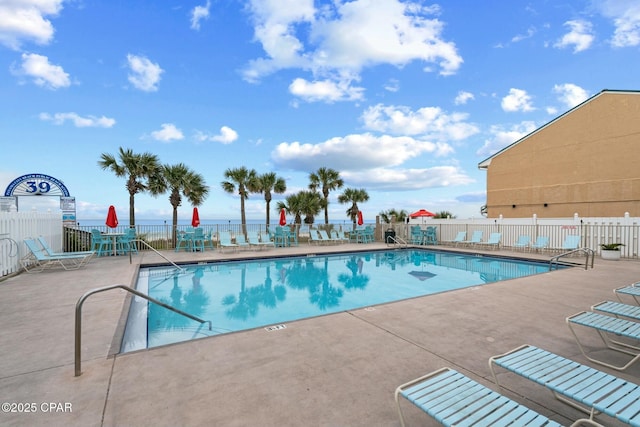 community pool featuring a patio, a water view, and fence