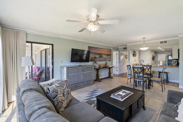 living room with ceiling fan, sink, a textured ceiling, light tile patterned floors, and ornamental molding