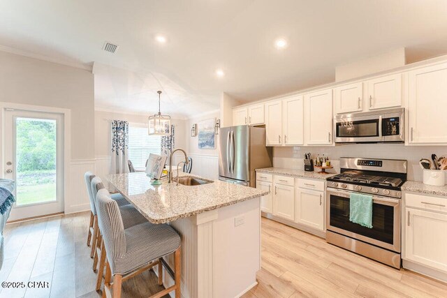 kitchen with white cabinets, appliances with stainless steel finishes, decorative light fixtures, and an island with sink