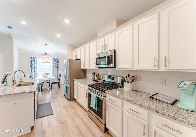 kitchen with sink, appliances with stainless steel finishes, pendant lighting, white cabinets, and light wood-type flooring