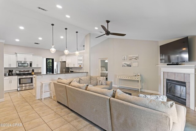 tiled living room with ceiling fan, a tile fireplace, and vaulted ceiling