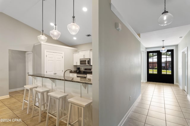 kitchen featuring white cabinetry, hanging light fixtures, stainless steel appliances, dark stone counters, and a breakfast bar