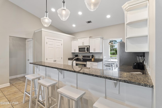 kitchen with appliances with stainless steel finishes, vaulted ceiling, pendant lighting, dark stone countertops, and white cabinetry