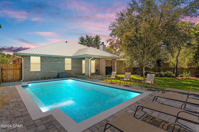 pool at dusk featuring a yard and a patio