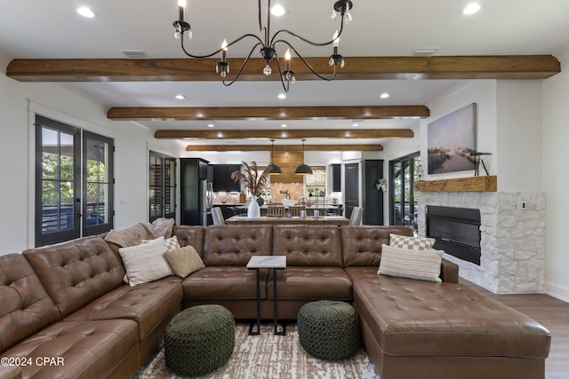 living room featuring beamed ceiling, wood-type flooring, a stone fireplace, and a notable chandelier