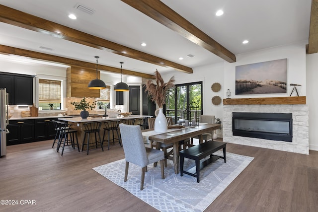 dining area featuring beam ceiling, dark hardwood / wood-style flooring, and a stone fireplace