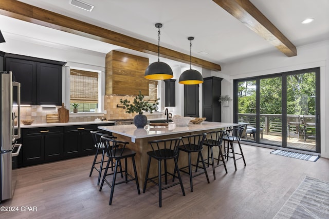 kitchen with pendant lighting, a breakfast bar, an island with sink, tasteful backsplash, and wood-type flooring