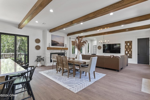 dining area featuring beamed ceiling, a notable chandelier, a stone fireplace, and light hardwood / wood-style flooring