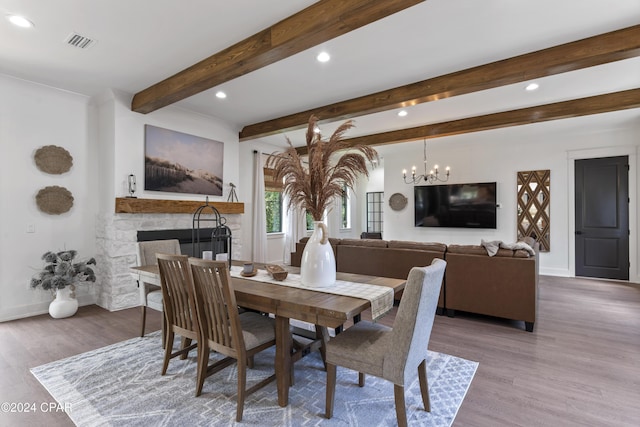 dining space with a stone fireplace, beamed ceiling, an inviting chandelier, and light wood-type flooring