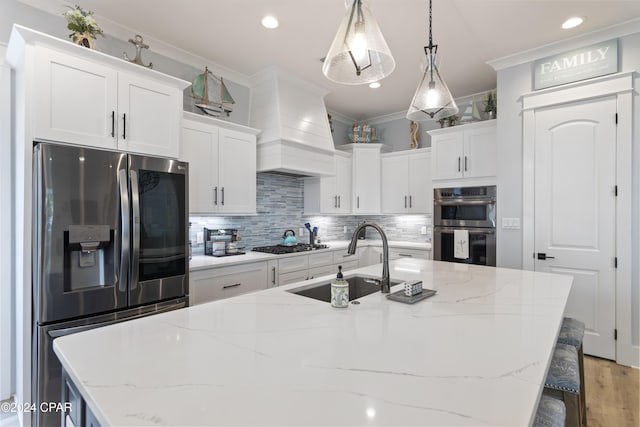 kitchen featuring white cabinetry, sink, stainless steel appliances, premium range hood, and pendant lighting