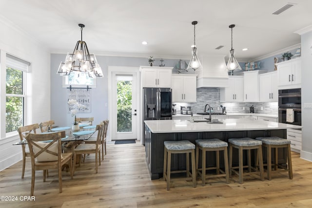 kitchen with a kitchen island with sink, decorative backsplash, appliances with stainless steel finishes, light hardwood / wood-style floors, and white cabinetry