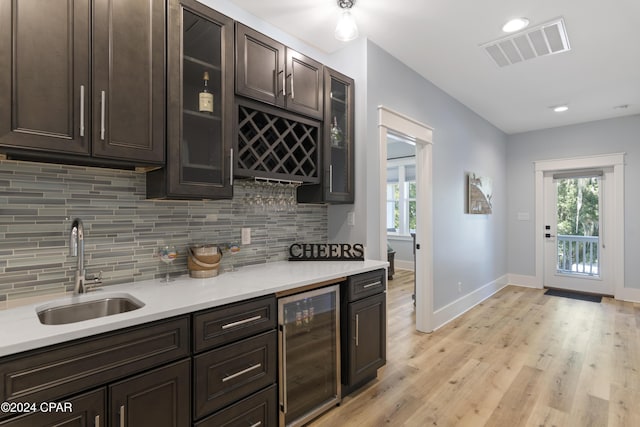 kitchen with dark brown cabinetry, sink, wine cooler, light hardwood / wood-style flooring, and backsplash