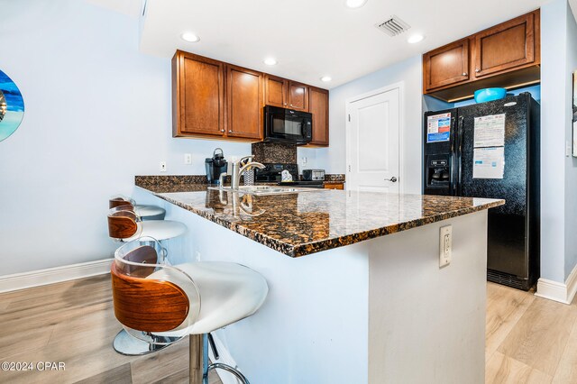 kitchen featuring black appliances, a kitchen breakfast bar, dark stone countertops, and sink