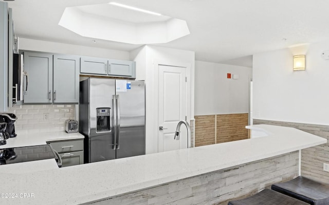 kitchen with gray cabinetry, light stone countertops, sink, stainless steel fridge with ice dispenser, and stove