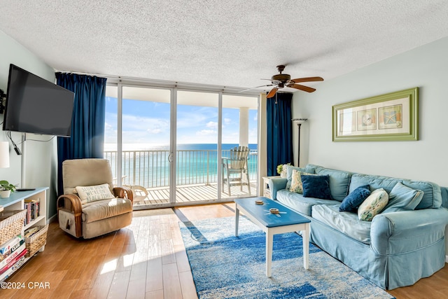 living room featuring hardwood / wood-style flooring, ceiling fan, a water view, expansive windows, and a textured ceiling