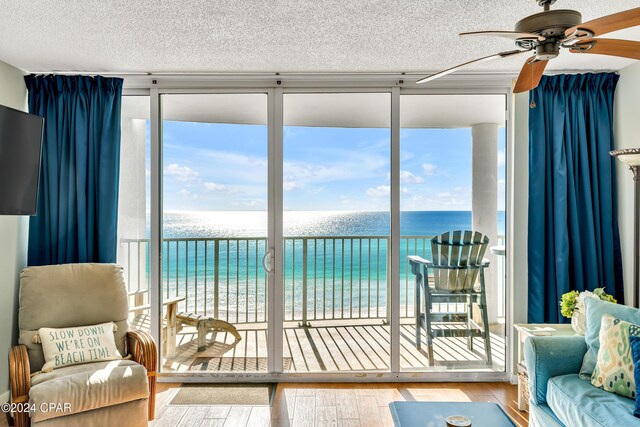 sunroom / solarium featuring a water view, ceiling fan, plenty of natural light, and a view of the beach