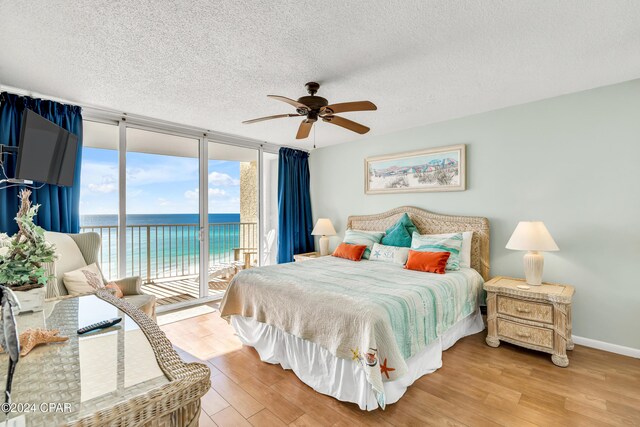 bedroom with ceiling fan, a wall of windows, access to outside, light wood-type flooring, and a water view