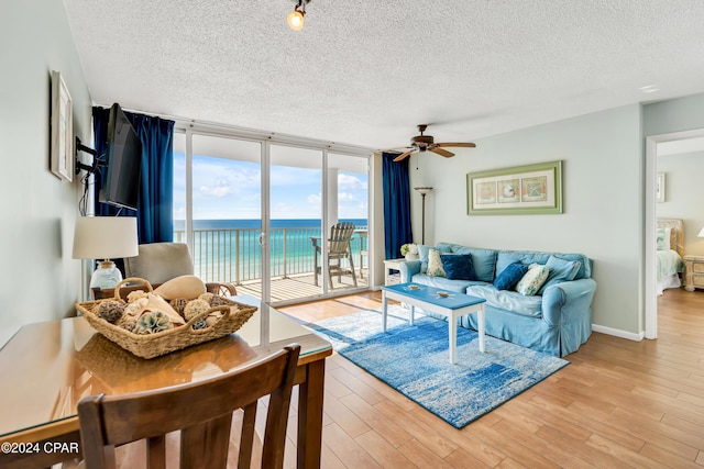 living room featuring a water view, expansive windows, a textured ceiling, and light wood-type flooring