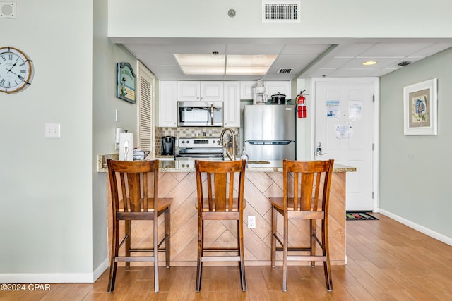 kitchen with a breakfast bar, appliances with stainless steel finishes, white cabinets, decorative backsplash, and kitchen peninsula