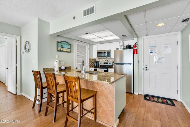 kitchen featuring backsplash, a kitchen breakfast bar, stainless steel appliances, white cabinets, and kitchen peninsula