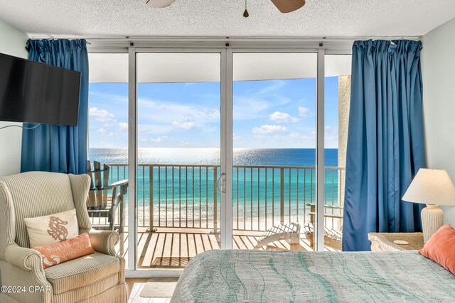 bedroom featuring a wall of windows, access to outside, a water view, a beach view, and a textured ceiling