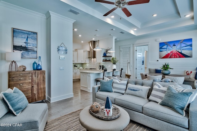 living room with a raised ceiling, ceiling fan, crown molding, and light hardwood / wood-style flooring