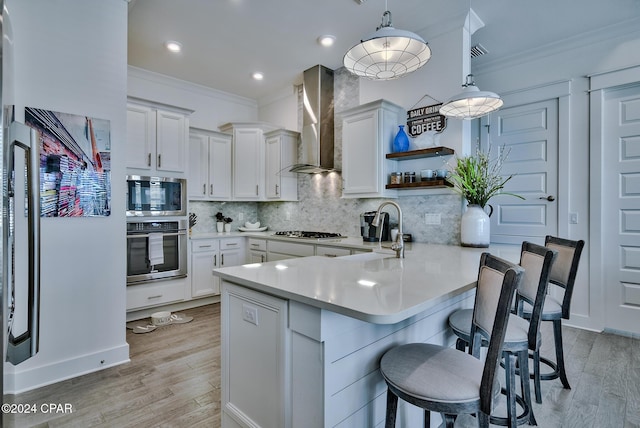 kitchen featuring white cabinets, wall chimney range hood, stainless steel appliances, and pendant lighting