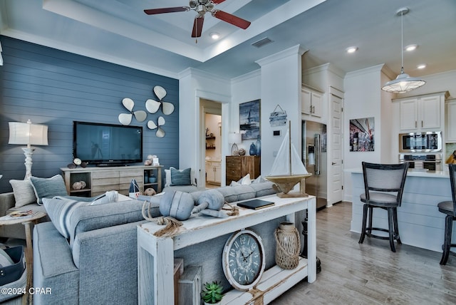 living room featuring light hardwood / wood-style floors, wooden walls, ceiling fan, a tray ceiling, and crown molding